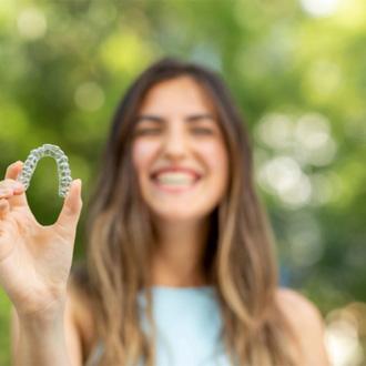  Woman smiling while holding Invisalign in Milford