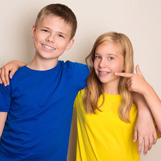 Two preteens pointing to smiles during pediatric orthodontic treatment