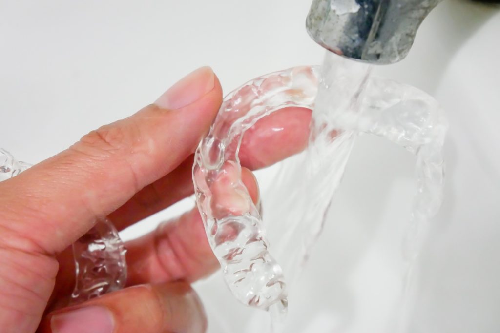 Patient rinsing Invisalign aligners in sink